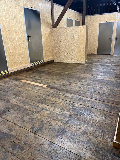 Gangbereich mit rustikalem Holzboden und Türen zu einzelnen Lagerboxen aus Holzspanplatten.