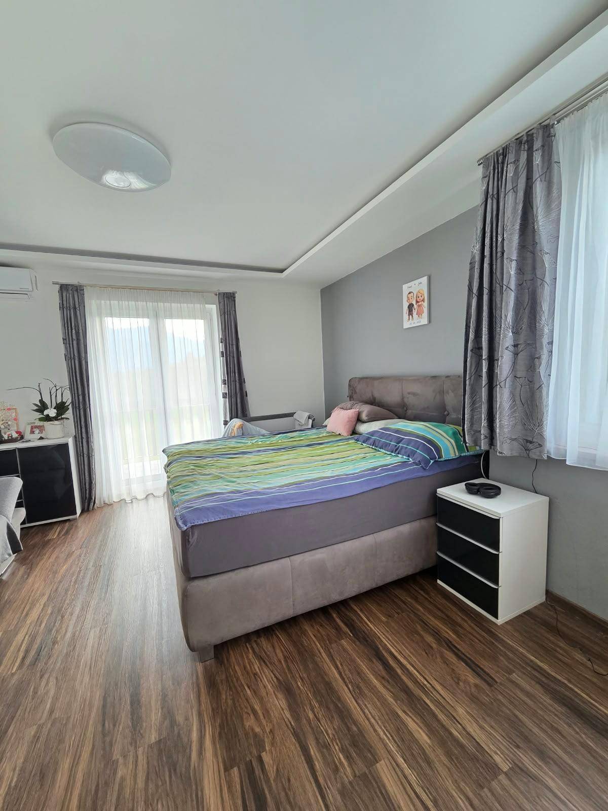Modernes Schlafzimmer mit Holzboden, großem Bett und Zugang zu einem Balkon.