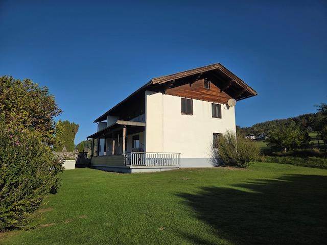 Freistehendes Einfamilienhaus mit traditionellem Satteldach und weitläufigem Rasenbereich unter blauem Himmel.