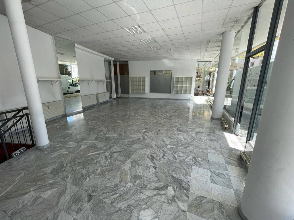 Weitläufiger Verkaufsraum mit glänzendem Marmorboden, hohen Decken und großen Fensterfronten zur Straße.