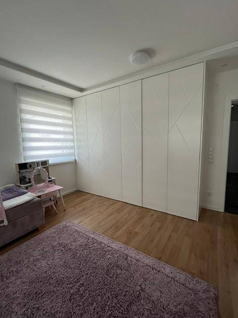 Geräumiges Kinderzimmer mit Holzboden und einer großen weißen Schrankwand.