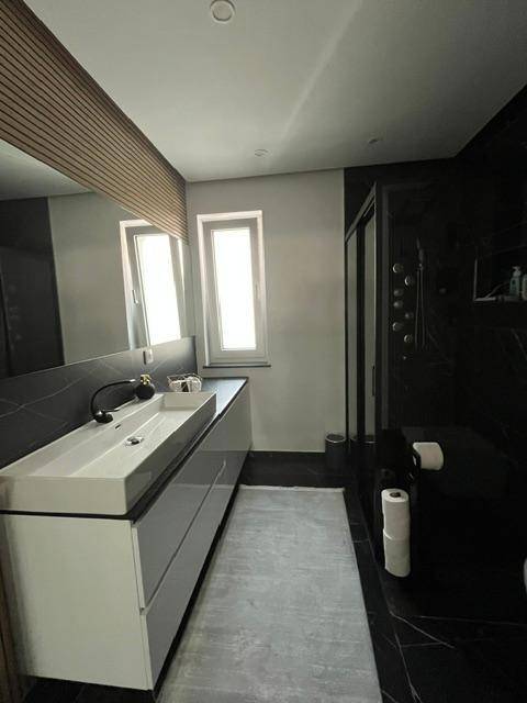 Elegantes Badezimmer mit Doppelwaschbecken, schwarzem Marmorboden und moderner Duschkabine.
