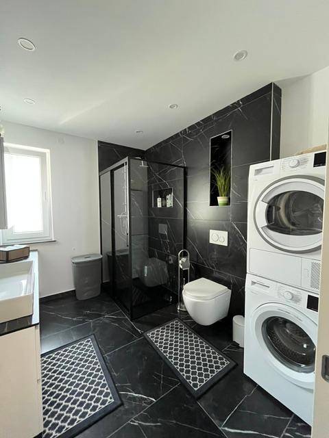 Elegantes Badezimmer mit schwarzem Marmorboden, Duschkabine, WC und Waschmaschine.