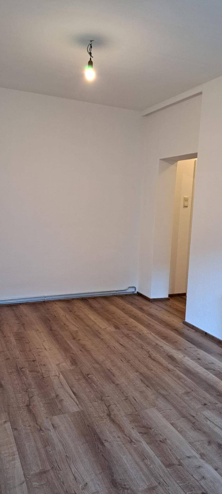 Leerer Raum mit modernem Laminatboden und weißen Wänden, bereit zur Einrichtung.