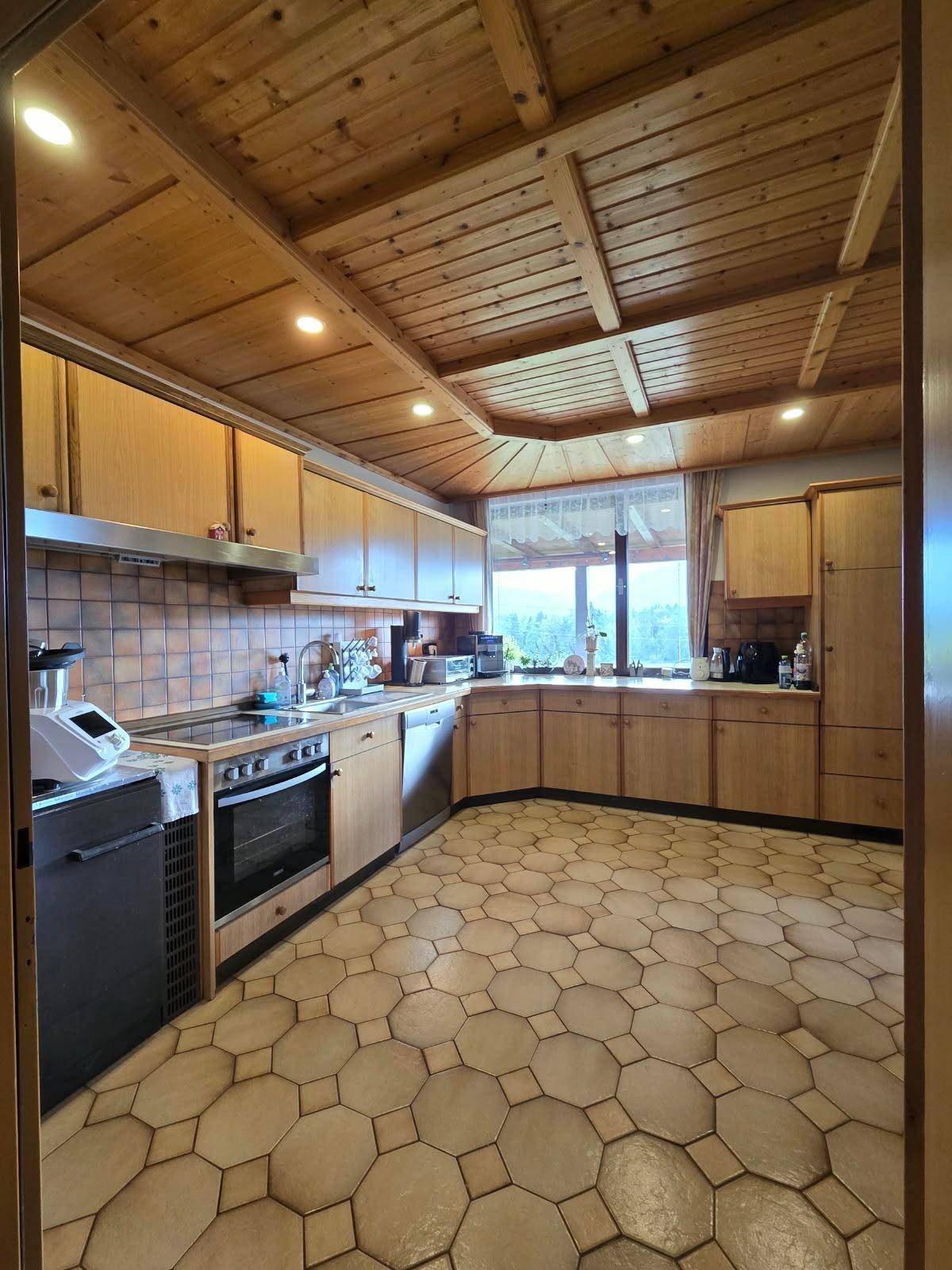 Geräumige Küche im Landhausstil mit Holzschränken, Fliesenboden und Blick ins Grüne.
