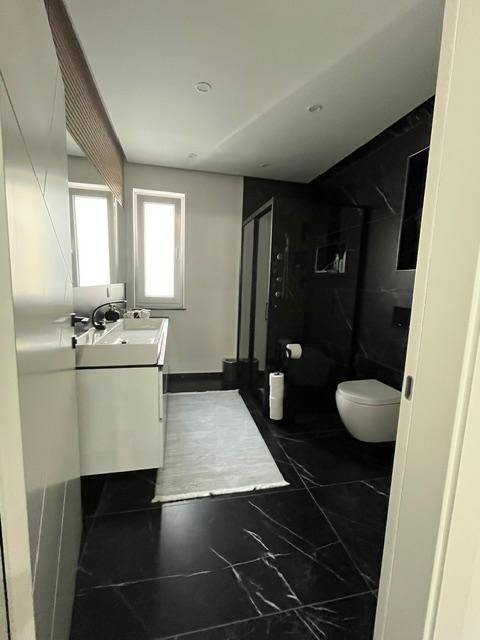 Modernes Badezimmer mit schwarzem Marmorboden, großem Waschtisch und Fenster für Tageslicht.
