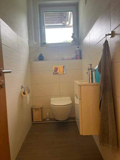 Modernes Gäste-WC mit wandhängender Toilette, kleinem Waschbecken und Fenster für Tageslicht.