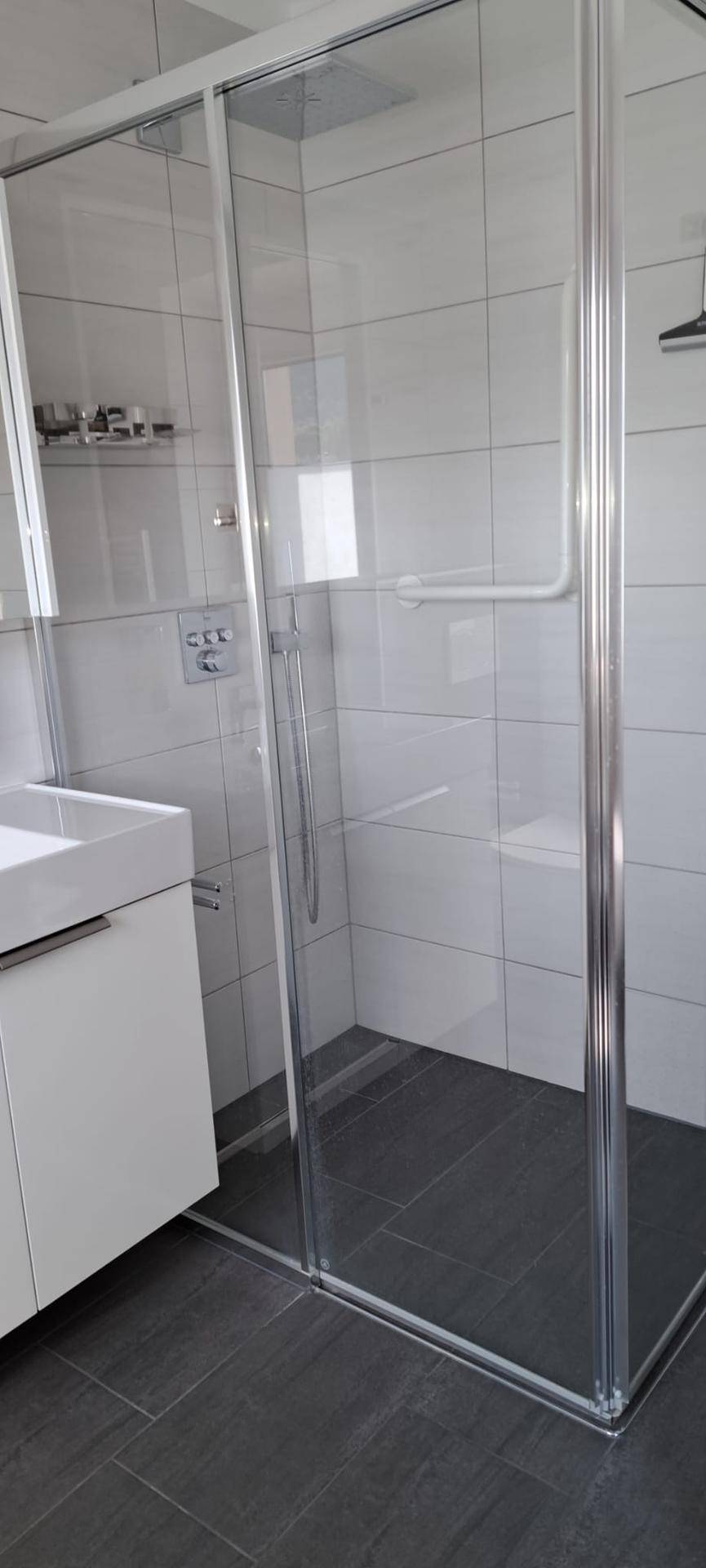 Moderne Duschkabine mit Glaswänden und Regendusche in einem gefliesten Badezimmer.