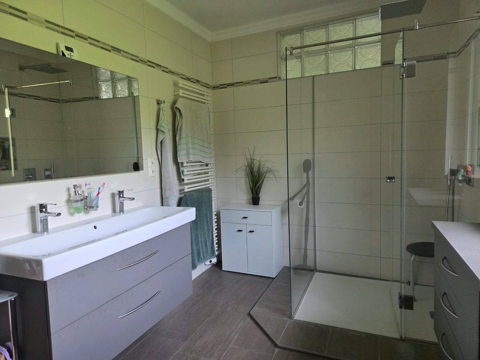Helles Badezimmer mit Doppelwaschbecken, großer Dusche und beheiztem Handtuchhalter.