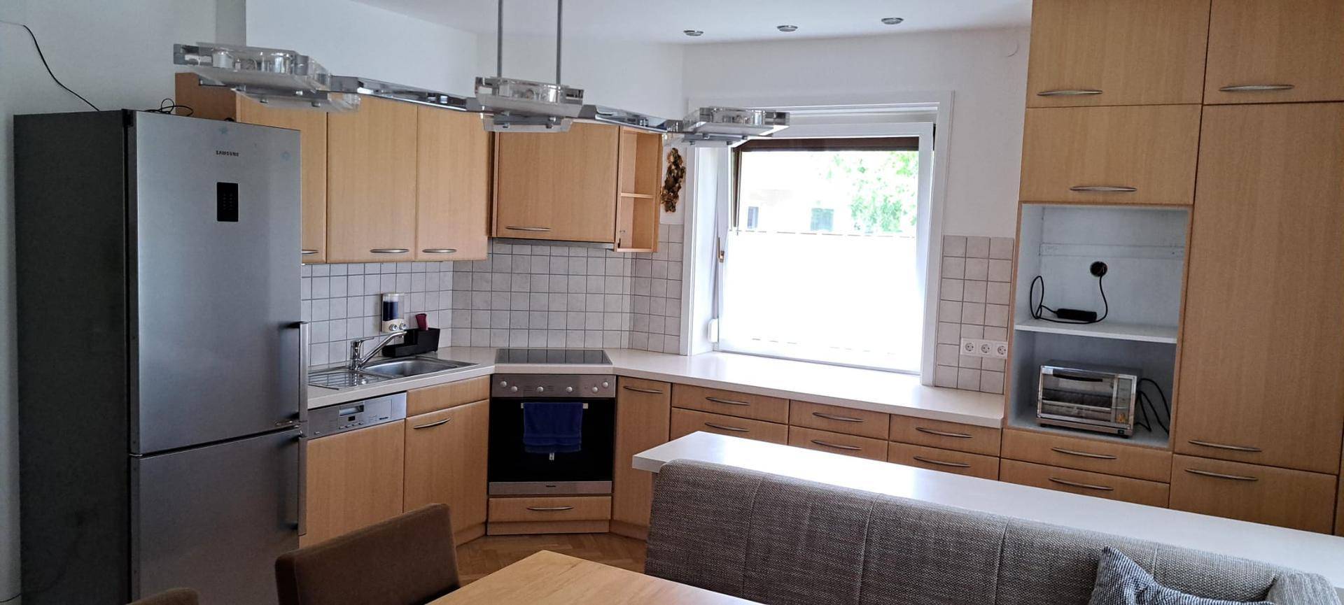 Helle Einbauküche mit Holzfronten, modernen Geräten und integriertem Essbereich am Fenster.