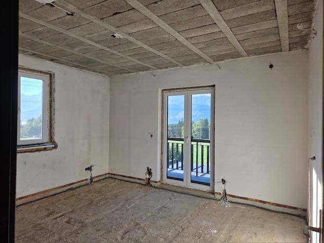Unfertiger Raum mit Rohbauwänden und Blick auf die Berge durch die Fenster.