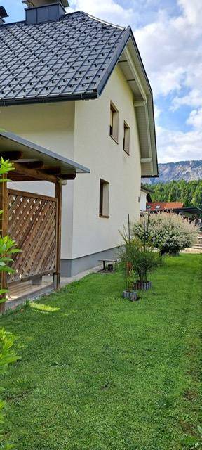 Seitenansicht des Hauses mit grünem Rasen und Holzverkleidung im Außenbereich.