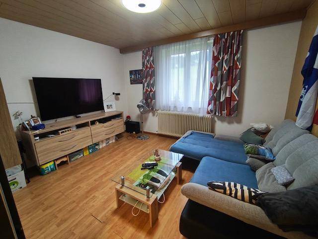 Gemütliches Wohnzimmer mit Holzboden, Sofa und Fernseher, dekoriert mit bunten Vorhängen.