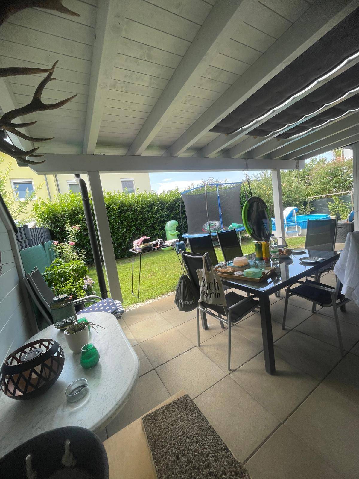 Überdachte Terrasse mit Essbereich und Blick auf den Garten mit Trampolin und Pool.