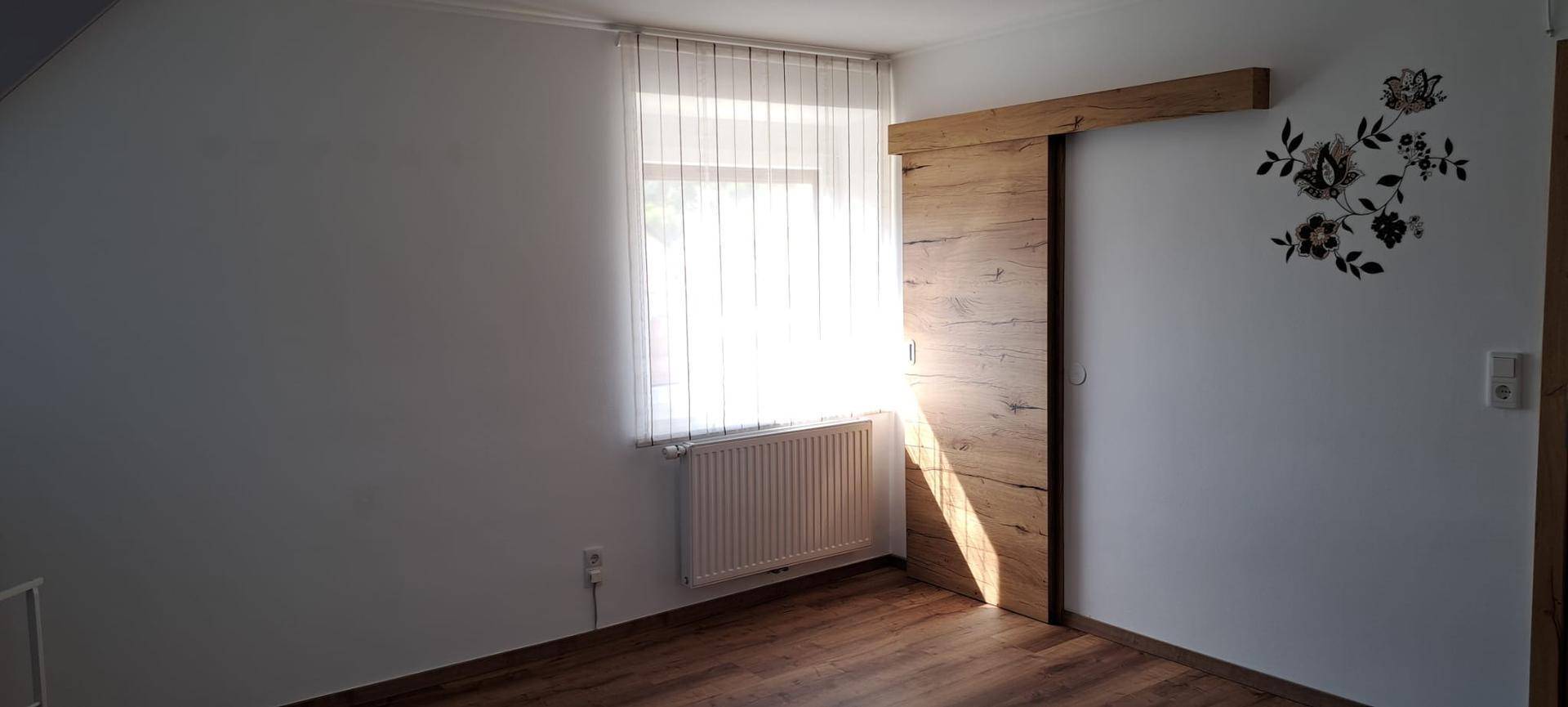 Heller Raum mit Fenster, Heizkörper und moderner Holzschiebetür, die viel Licht hereinlässt.