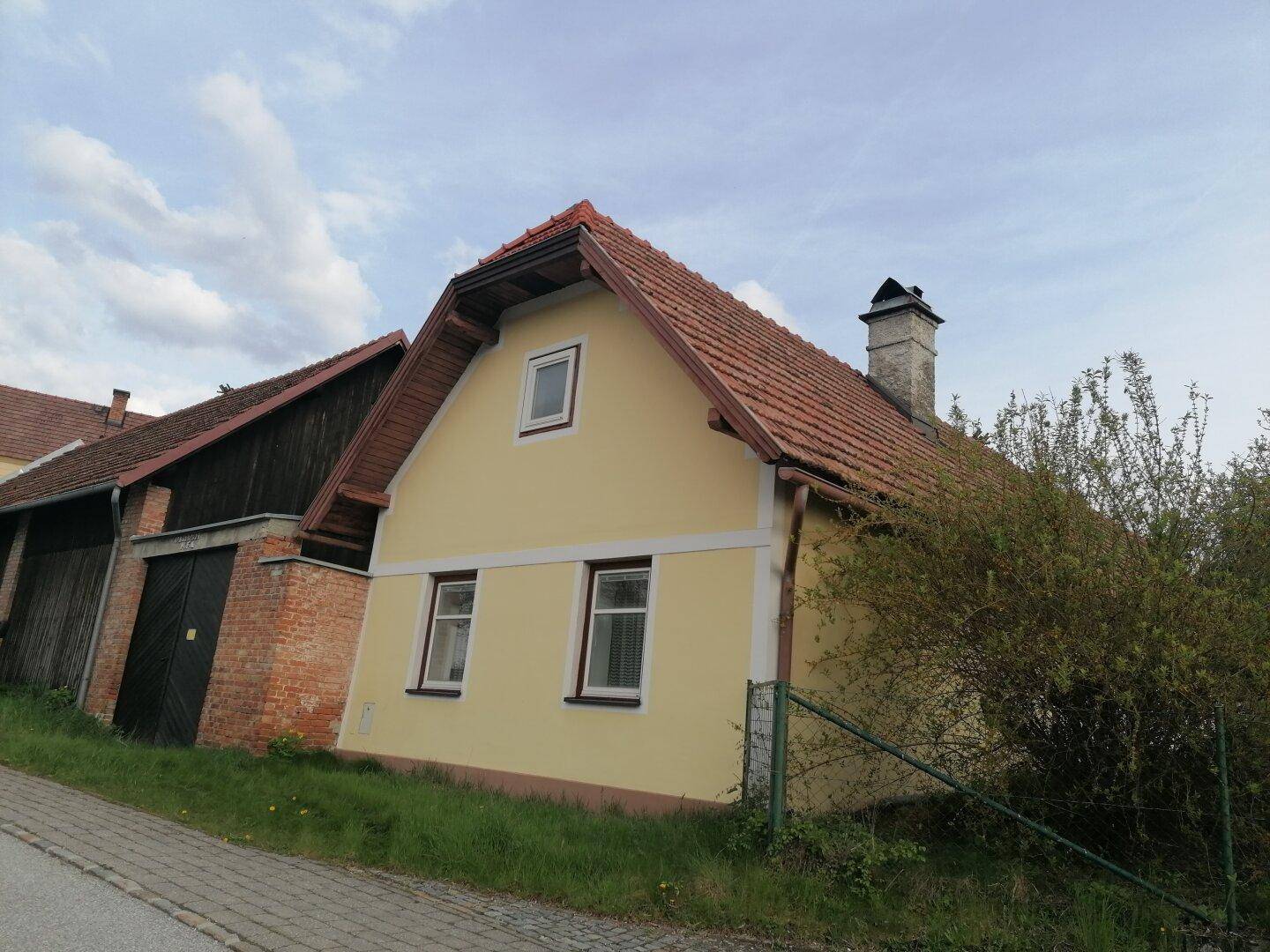 Traditionelles gelbes Haus mit rotem Ziegeldach und einem hohen Schornstein, umgeben von Grün.