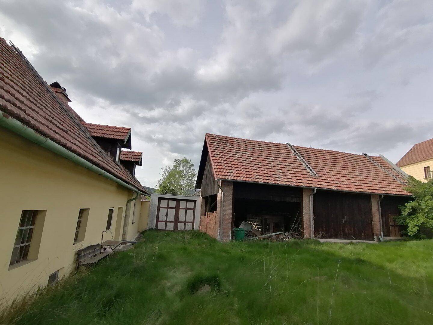 Ansicht des gelben Hauses und einer großen Scheune mit offenem Bereich, getrennt durch ein kleineres Gebäude.