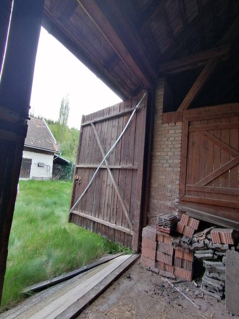 Innenansicht einer Scheune mit offener Holztür, Blick auf das Haus und die grüne Landschaft.