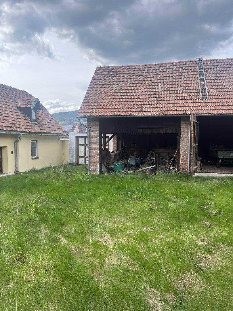 Gesamtansicht des gelben Hauses und der Scheune, getrennt durch eine weitläufige grüne Wiese.