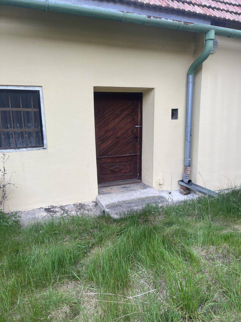Nahaufnahme einer rustikalen Holztür am gelben Haus mit einem kleinen Fenster daneben.