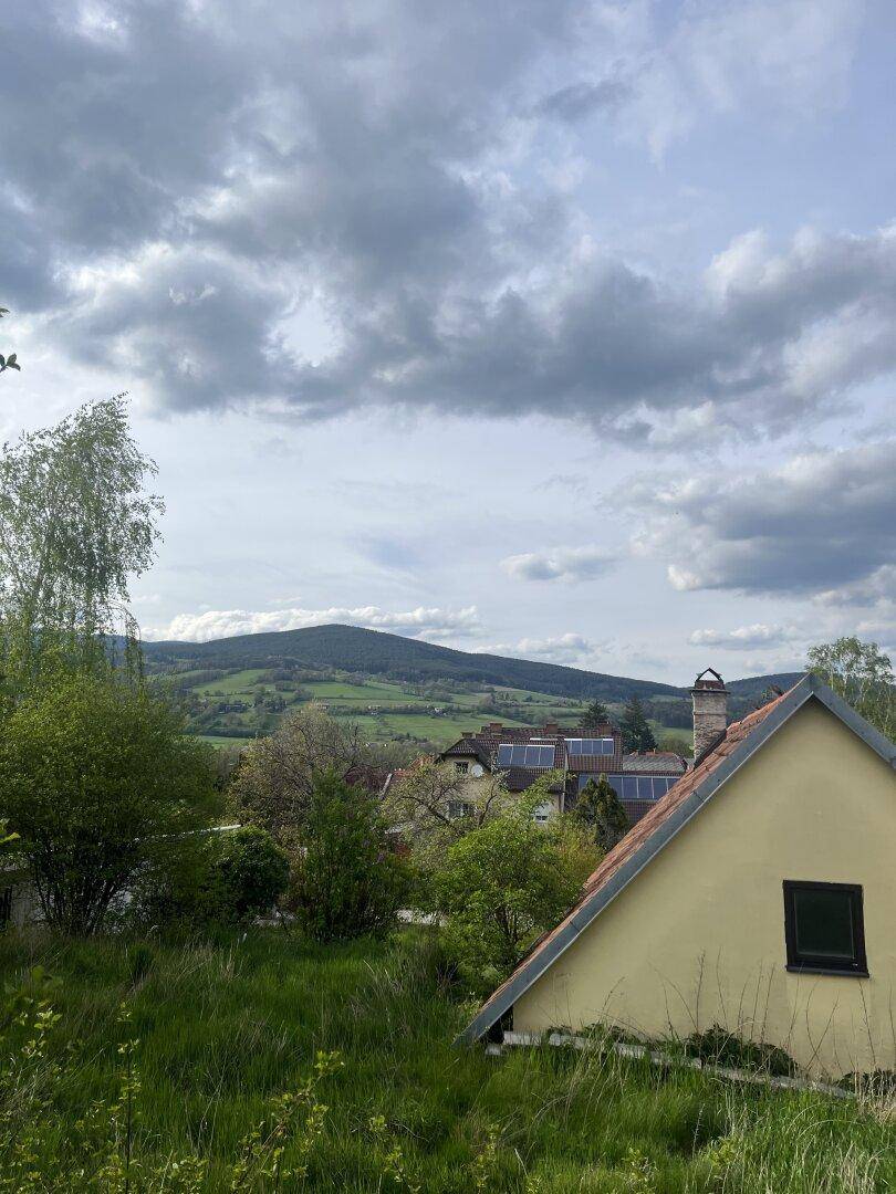 Panoramablick auf eine grüne Hügellandschaft mit Bergen in der Ferne, teilweise mit dem Haus.
