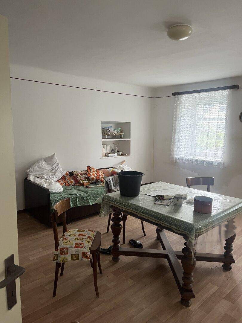Schlafzimmer mit Bett, Tisch und Stühlen, einfacher Einrichtung und renovierungsbedürftigem Zustand.