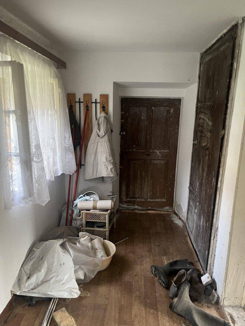Flur mit Holzboden, zwei alten Holztüren und einem Fenster, das Tageslicht hereinlässt.