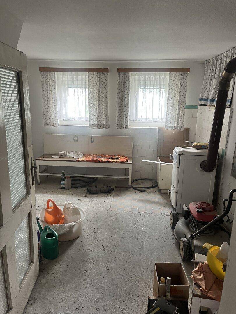 Geräumiger Hauswirtschaftsraum mit Betonboden, zwei Fenstern und verschiedenen Geräten, inklusive Rasenmäher.