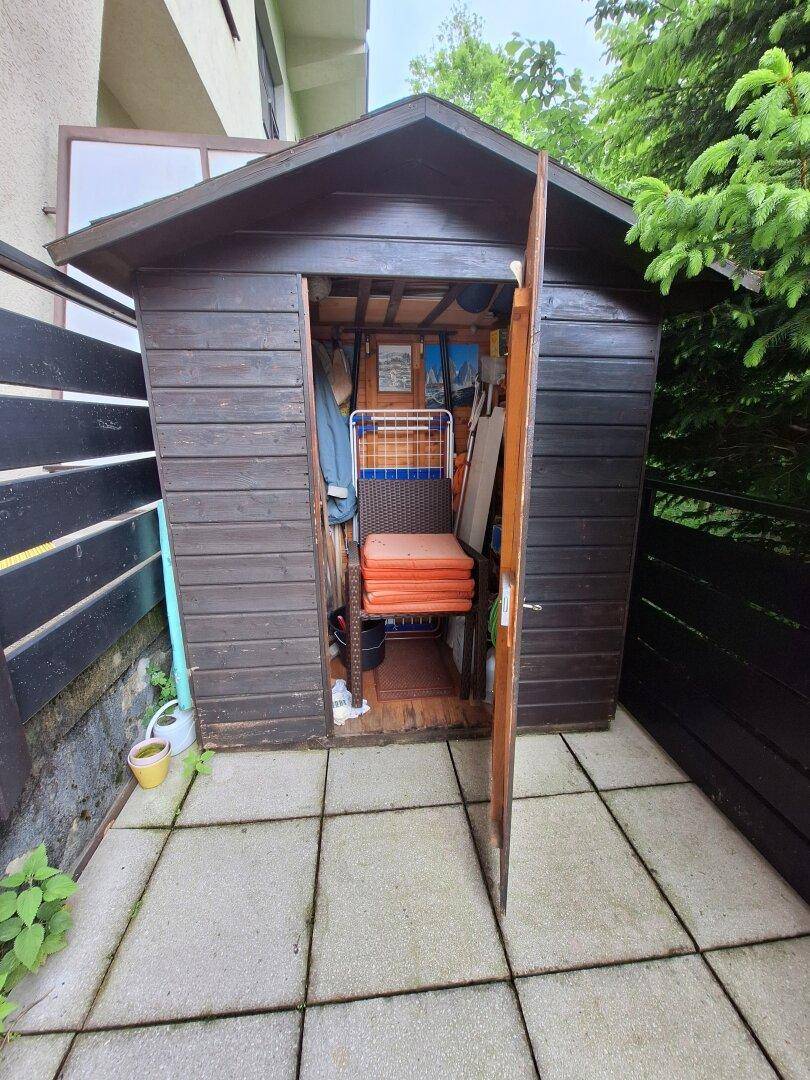 Kleiner Holzschuppen im Garten auf gepflastertem Bereich für Gartengeräte und Lagerung.