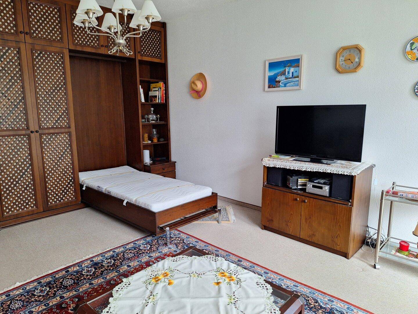 Gemütliches Wohnzimmer mit ausklappbarem Bett, Teppichboden und traditionellen Holzmöbeln.