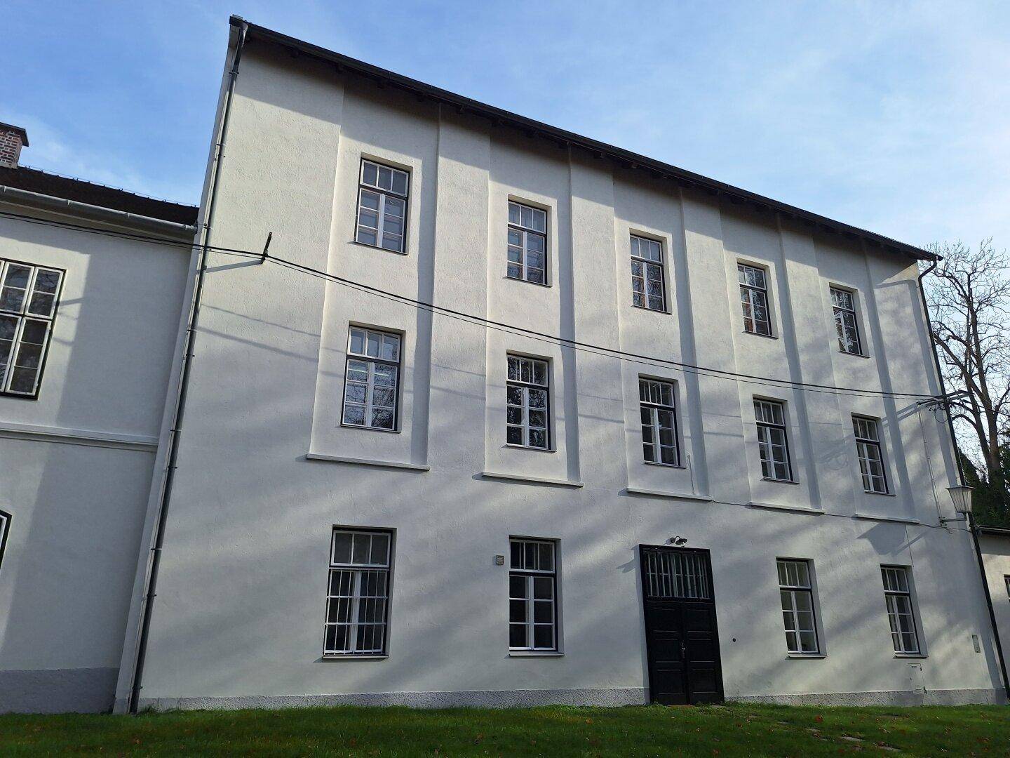 Seitenansicht eines großen Gebäudes mit vielen Fenstern und einer schlichten, hellen Fassade.