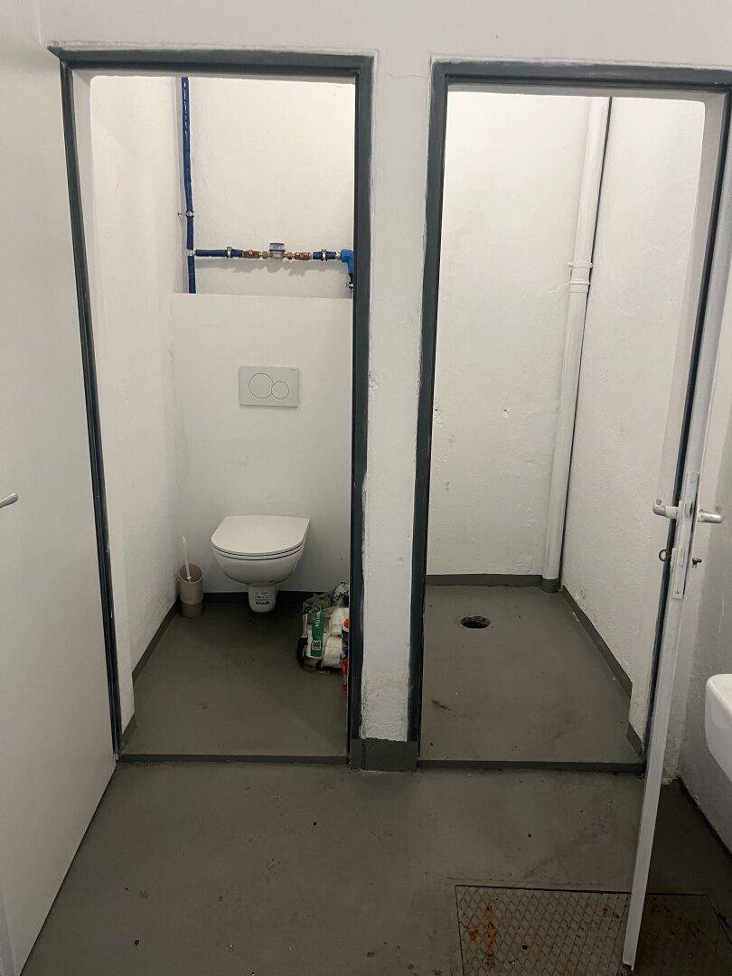 Zwei separate Bereiche, einer mit wandhängender Toilette und der andere als Duschbereich mit Bodenablauf.