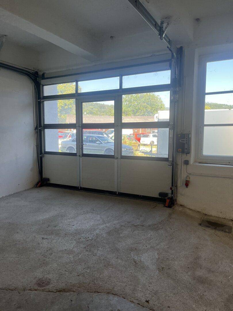 Innenansicht einer Garage mit einem großen, teilweise geöffneten Sektionaltor und Betonboden.