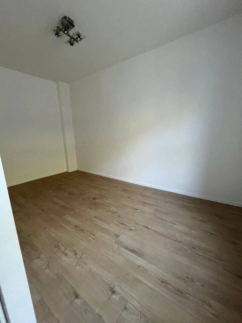 Leerer Raum mit hellem Holzfußboden und weißen Wänden, bereit zur individuellen Gestaltung.