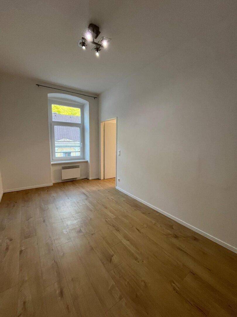 Heller Raum mit Holzfußboden und einem Fenster, das Tageslicht hereinlässt.