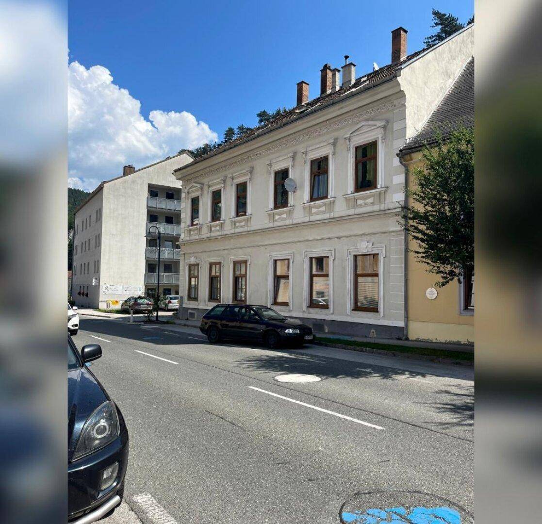 Historisches Gebäude mit klassischer Fassade an einer städtischen Straße mit parkenden Autos.