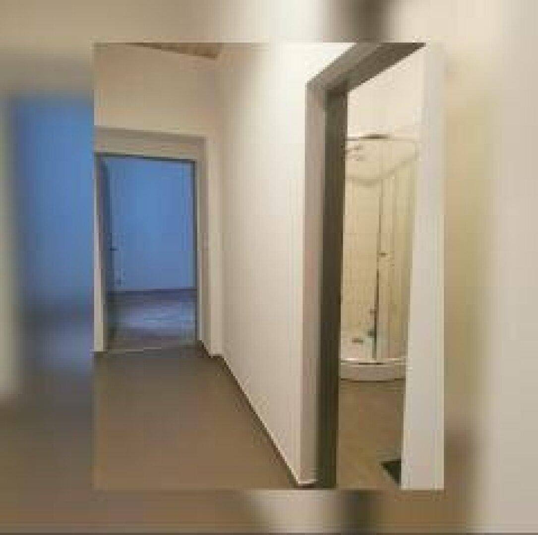 Flur mit hellem Laminatboden und Blick in ein Badezimmer mit Duschkabine.