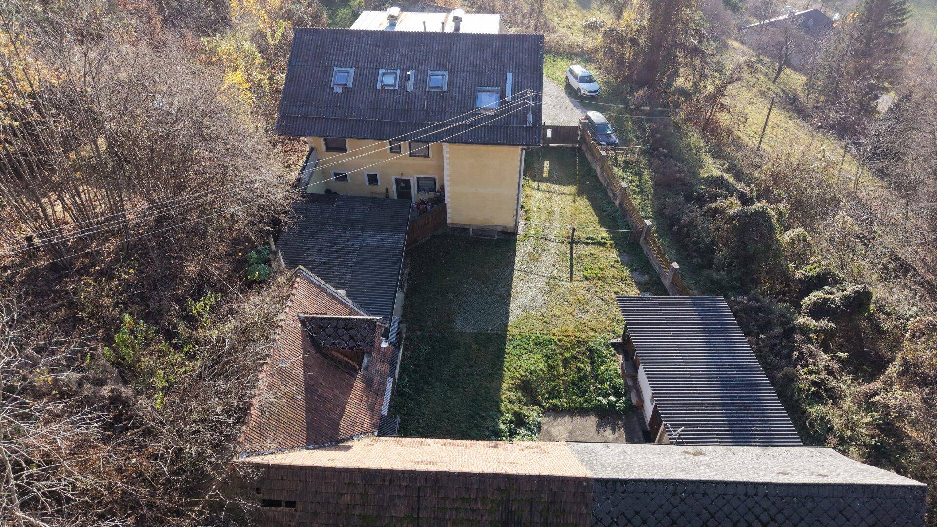 Rückansicht des Wohnhauses mit Gartenbereich, Nebengebäuden und angrenzendem Wald.