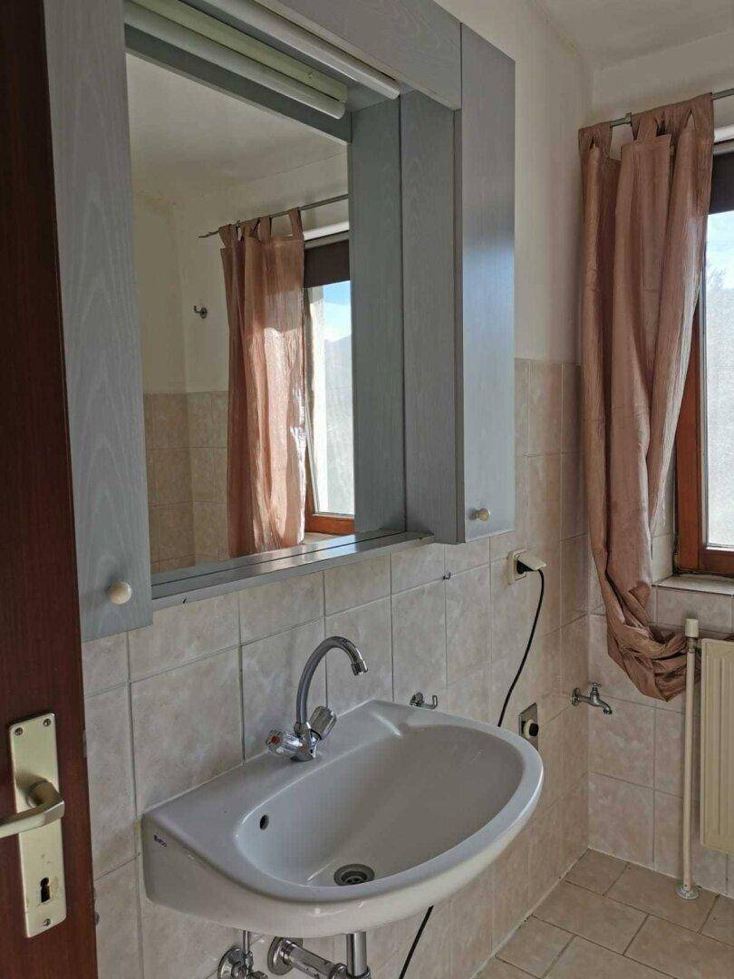 Helles Badezimmer mit Fliesenboden, Waschbecken, Spiegelschrank und Fenster.