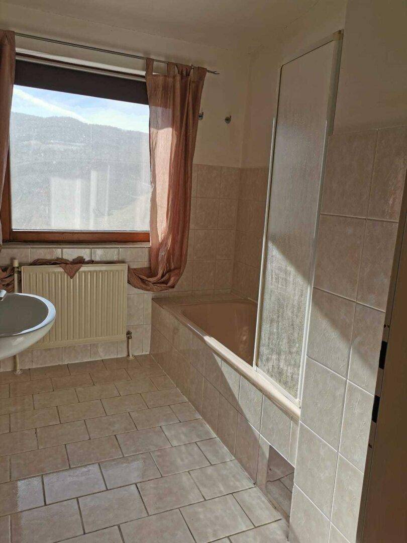 Badezimmer mit Badewanne, Duschabtrennung, Waschbecken und Fenster mit Bergblick.