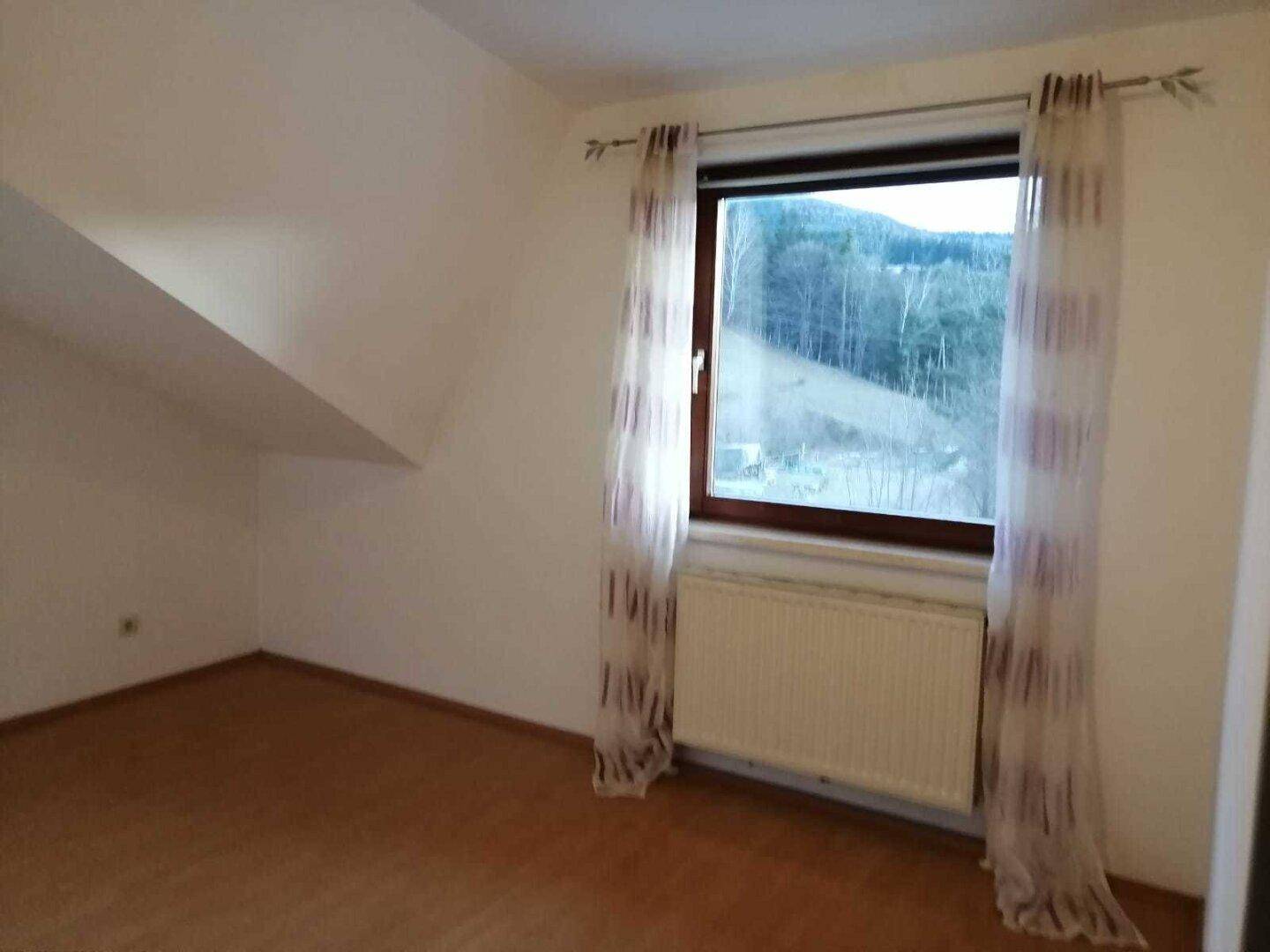 Schlafzimmer im Dachgeschoss mit Laminatboden, Dachschräge und Fenster mit Blick ins Grüne.