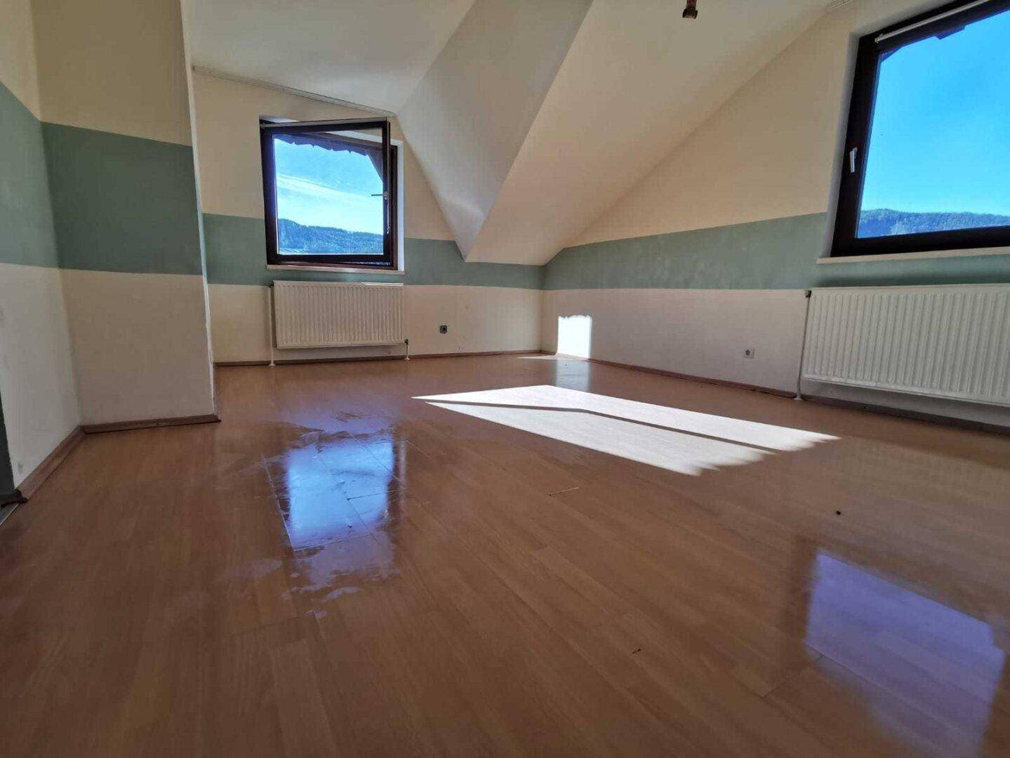 Heller Raum im Dachgeschoss mit Laminatboden, Dachschrägen und zwei Fenstern.