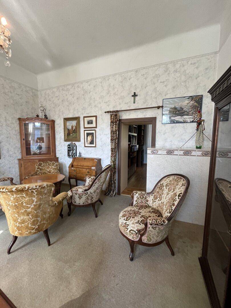 Klassisch eingerichtetes Wohnzimmer mit gemusterten Sesseln und Blick in einen weiteren Raum.