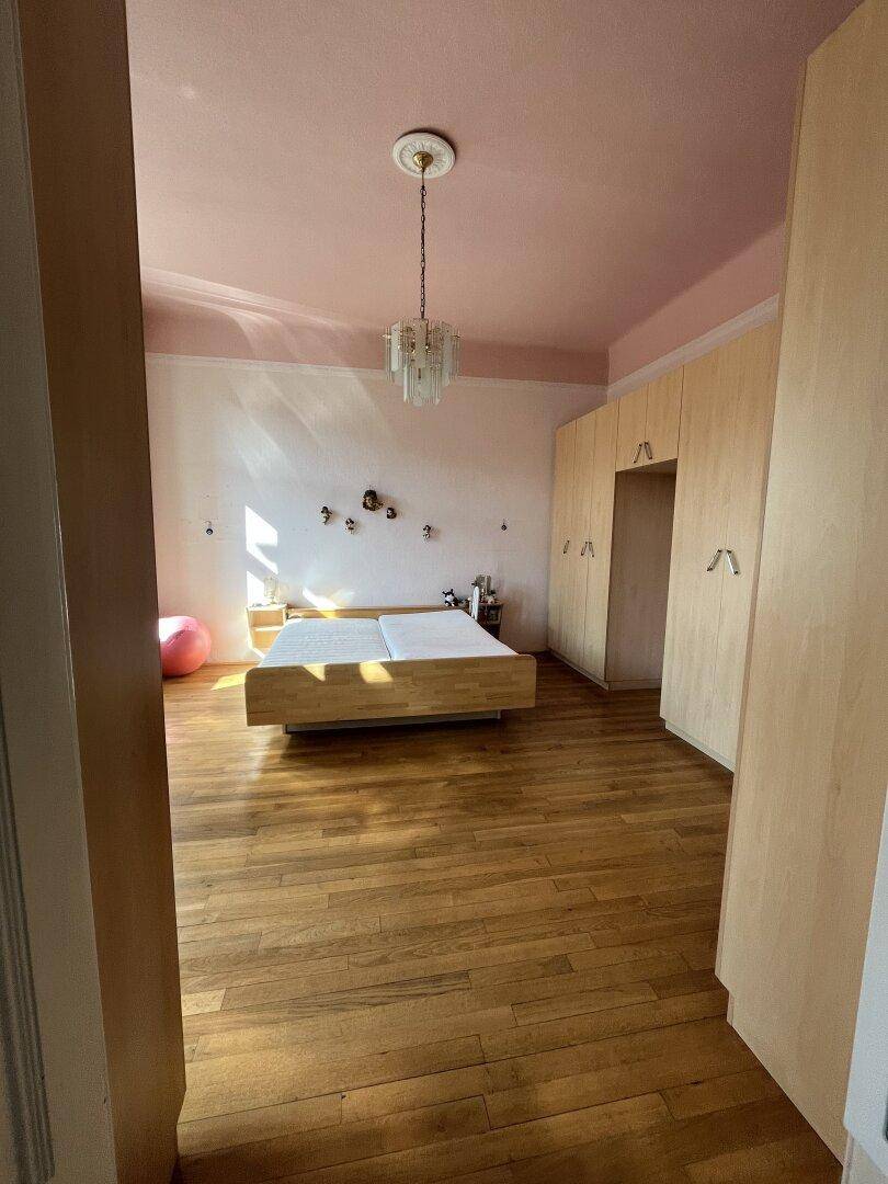 Helles Schlafzimmer mit Holzboden, Einbauschränken und rosa Decke.