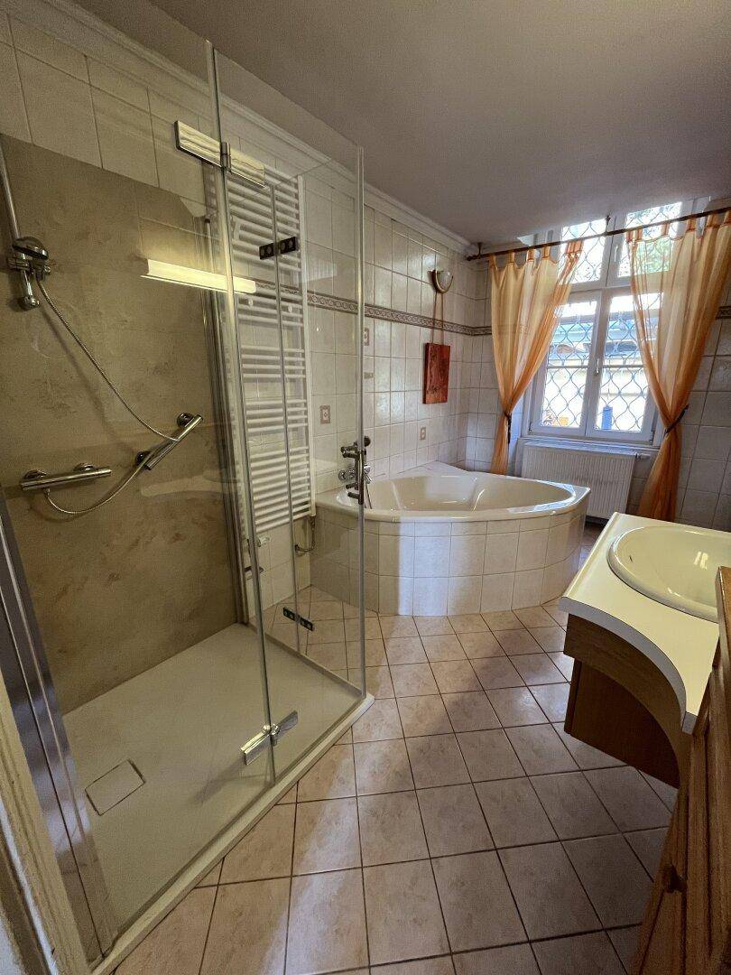 Gefliestes Badezimmer mit Dusche, Eckbadewanne und Fenster.
