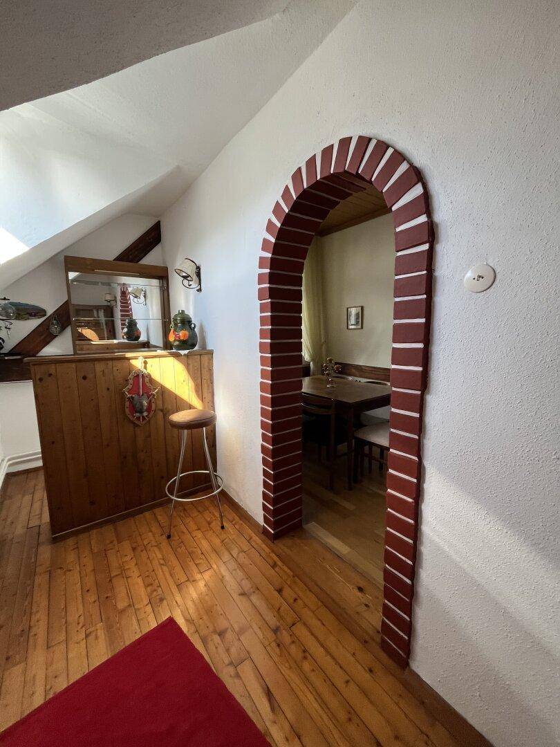 Dachgeschossbereich mit kleiner Bar, Holzboden und Ziegelbogen.