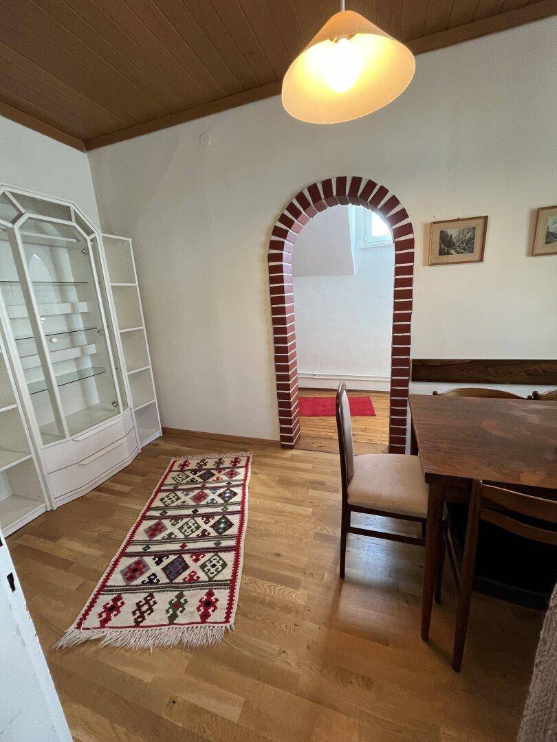 Esszimmer mit Holzboden, weißem Schrank und Blick durch einen Ziegelbogen.