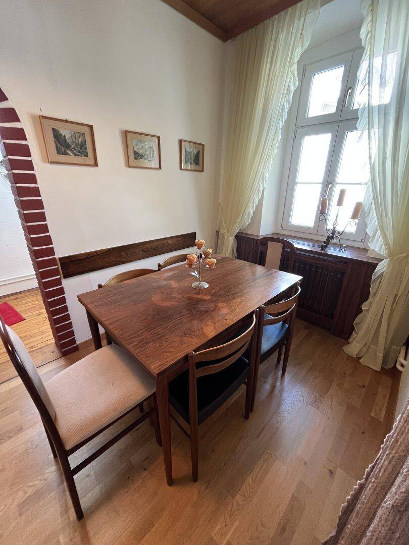 Helles Esszimmer mit Holztisch, Stühlen und großen Fenstern.