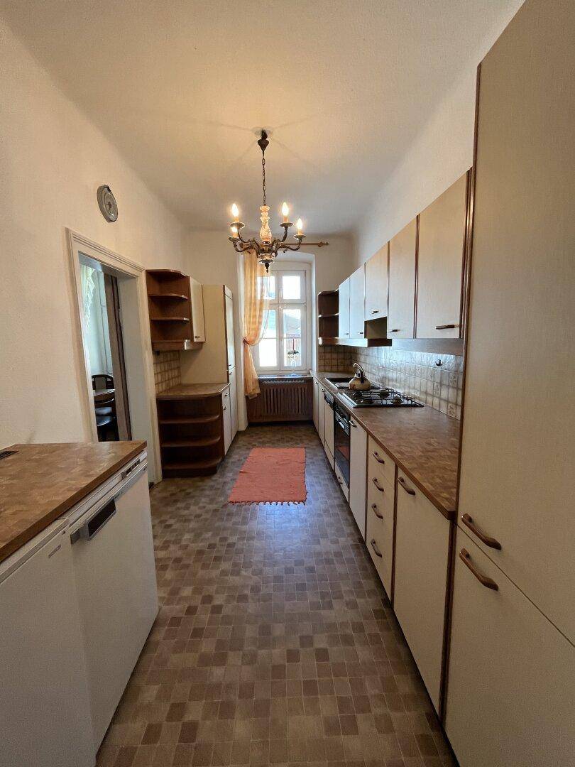 Schmale Küche mit älteren Einbauschränken, Holz-Arbeitsplatten und Fenster.