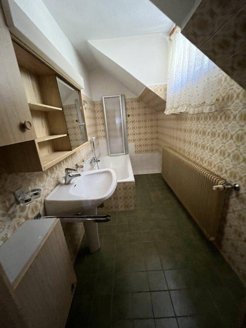 Badezimmer im Dachgeschoss mit Badewanne, Waschbecken und gemusterten Fliesen.